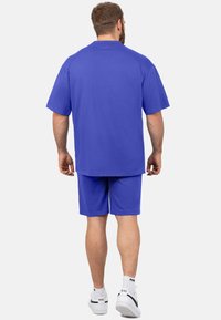 Ensemble sportif bleu composé d'un t-shirt ample à manches courtes et d'un short en tissu léger, accompagné de baskets blanches.