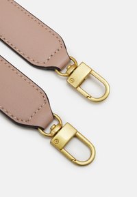 Vaaleanruskeat nahkahihnat, joissa on yksityiskohtainen ommel ja kultaiset metalliset pyörivät lukot valkoisella taustalla.