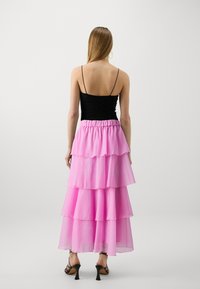 Svart spetstopp med tynne stropper, kombinert med en lagdelt rosa chiffon skjørt, som har rynkede detaljer og elastisk midje.