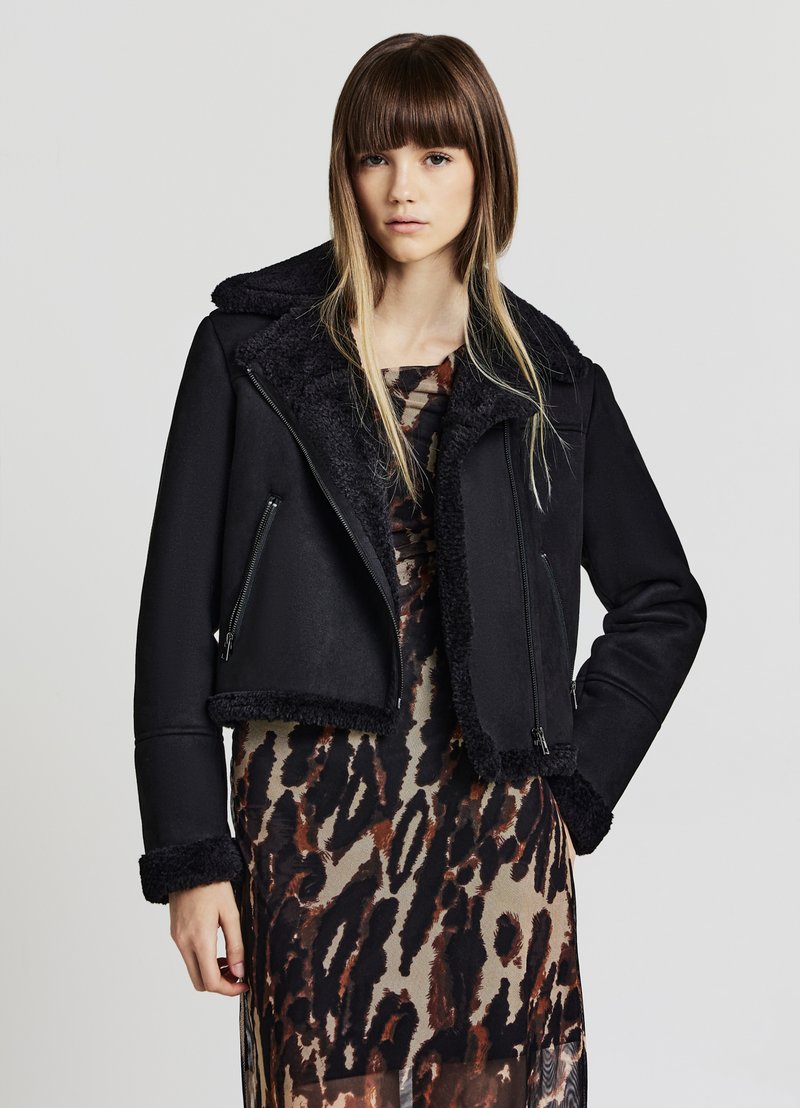 Giacca nera corta con colletto e polsini in pelliccia, dotata di tasche frontali con zip e una superficie esterna liscia.