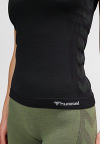 Nahaufnahme einer Person, die ein schwarzes hummel Sporttop und grüne Leggings mit einem strukturierten Chevron-Muster an den Seiten trägt.