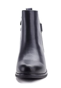 Bottine noire cheville avec une finition synthétique lisse, bout rond et un détail de sangle sur le côté. Semelle plate et design minimaliste.
