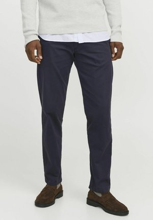 Marineblaue Chinos aus Baumwollmischgewebe mit geradem Schnitt und Seitentaschen. Kombiniert mit braunen Wildlederschuhen und einem grauen Strickpullover.