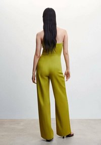 Zelený overal bez ramínek s širokými nohavicemi, vyrobený z hladkého materiálu a s ladným střihem. Minimalistický styl bez viditelných vzorů.