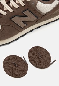 Smeđi nubuk i mrežasti tenisice s bež naglaskom, sa zaokrugljenim smešnim vezicama smeđe boje i crnim gumenim potplatom s teksturiranim gripom.