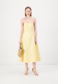 Dzeltena midi kleita ar plānām siksniņām, A formas siluets, sānu kabatas un gluda tekstūra. Apvienota ar austu somu un dabīgu krāsu augstpapēžu kurpēm.