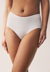 Culotte hipster blanche en coton avec une taille élastique lisse, dotée d'un design sans coutures et d'une texture douce, posée sur un fond neutre.
