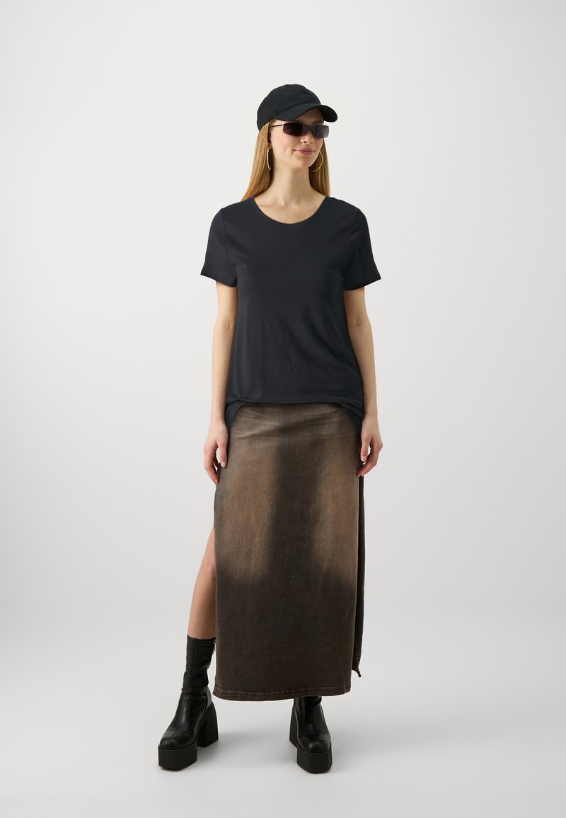 Maglietta nera a maniche corte abbinata a una gonna di jeans marrone con uno spacco laterale, indossata con stivali neri con plateau e un cappellino nero.