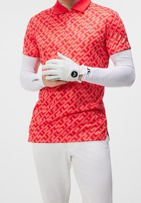 Polo de golf de patrón rojo con cuello, mangas cortas y una capa base blanca de manga larga debajo. Guantes de golf blancos con detalle de logo.