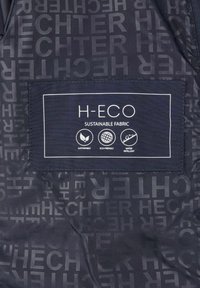 Schwarzer Stoff mit wiederholtem Textmuster, das "HECHTER" liest. Enthält ein weißes Etikett mit der Aufschrift "H-ECO" sowie Symbole für nachhaltig, umweltfreundlich und wasserabweisend.