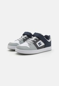Baskets grises et bleu marine avec une finition texturée, dotées d'une sangle Velcro, d'une semelle en caoutchouc blanche et d'un logo distinct sur le côté.