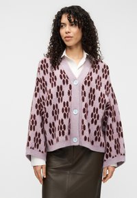 Λιλά ζακέτα με μοτίβο μπορντό πατουσάκια, με V λαιμόκοψη, τρία μπλε κουμπιά και ριμπ μανσέτες, συνδυασμένη με καφέ δερμάτινη φούστα.