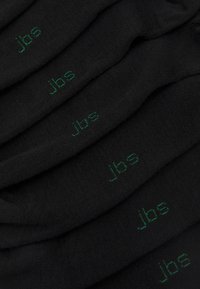 Schwarze Socken mit glatter Textur, die mit "jbs" in Grün bestickt sind. Mehrere Paare sind übereinander gestapelt, was die Marke prominent zur Geltung bringt.