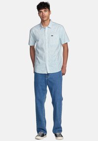 Short-sleeve, light blue button-up shirt with a subtle pattern, left chest pocket, paired with blue jeans and black sneakers.