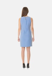 Abito senza maniche di colore azzurro chiaro con un collo alto, dettaglio a chiave sulla schiena e silhouette aderente, abbinato a scarpe nere con tacco alto.
