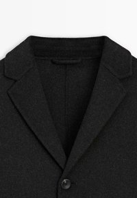 Blazer in lana nera con revers a punta, chiusura a un bottone e tessuto texturizzato con finitura morbida.