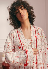 Biely látkový kimono s červenými akcentmi, s hravým potlačeným vzorom nápojov, srdiec a kvetín, dlhými rukávmi a voľným strihom.