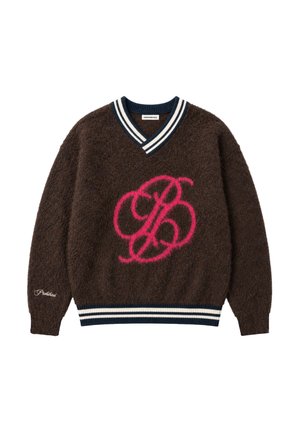 Homme portant un pull marron doux avec un motif rose en écriture et un bonnet en tricot bleu, regardant sur le côté avec les mains jointes devant lui.