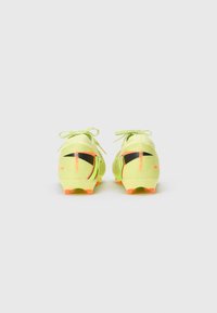 Botas de fútbol color verde lima con detalles en negro y naranja, con un diseño texturizado. De perfil bajo con punta redondeada y suela flexible.