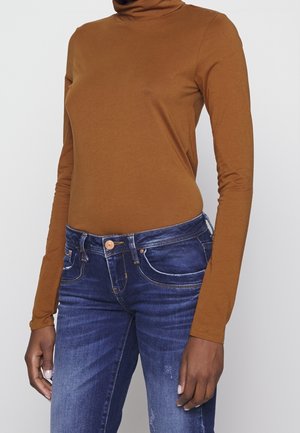 Bruine coltrui met lange mouwen gecombineerd met vervaagde blauwe jeans, voorzien van een gulp met knopen en een klassieke vijfzakkenstijl. Zachte, rekbare stof.