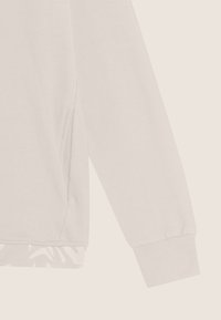 Manica di felpa grigia chiara con polsino a costine, caratterizzata da una spaccatura laterale per il comfort e un sottile motivo floreale lungo l'orlo.