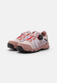 Chaussures de sport roses claires avec des lacets rouges contrastants, tige en maille texturée, semelle extérieure en caoutchouc noir et fermeture à cadran réglable.