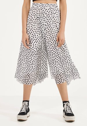 Witte wide-leg cropped broek met zwarte polkadots, gedragen met zwart-witte hoge sneakers, getoond van taille tot voeten.