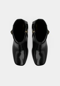 Mustad mustad põlvekõrgused saapad, millel on siledisain, teravad varbad ja kuldse riistvaraga aksessuaarid. Sile tekstuur läikiva viimistlusega.