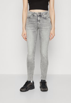 Grå skinny jeans med en falmet vask, fem lommer og knaplukning. Bæres med sorte sneakers med grå accenter.
