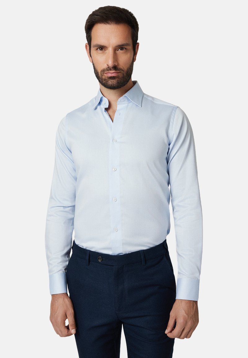 Jasnoniebieska koszula na guziki z długimi rękawami, klasycznym kołnierzykiem i gładką fakturą, zestawiona z ciemnogranatowymi spodniami.
