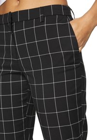 Black checkered pants featuring white grid lines, flat front, diagonal side pockets, and a smooth fabric texture.