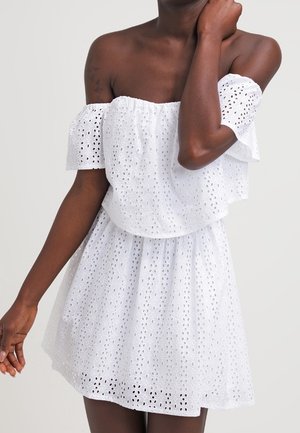 Schulterfreies weißes Augellochspitzenkleid mit gerafftem Oberteil und elastischer Taille, getragen von einer Person mit dunklem Hautton.
