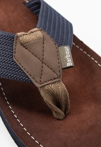 Sandal cu talpă groasă, în nuanțe de marron și bleumarin, cu bretele din textil împletit. Prezintă o pată accent maronie și un etichete cu textul "Barbour".