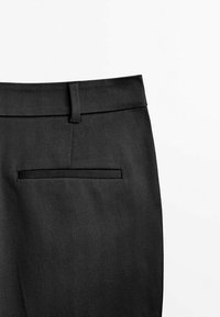 Section de pantalon formel noir montrant une ceinture avec passants et une seule poche passepoilée arrière côté droit.