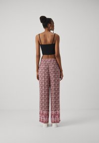 Top corto nero e pantaloni leggeri a gamba larga con un motivo floreale rosa e un bordo bianco. I pantaloni hanno una vita elasticizzata.