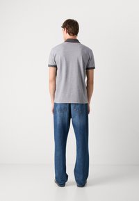 Γκρίζο κοντομάνικο πόλο μπλουζάκι με σκούρο γιακά και μανίκια, συνδυασμένο με χαλαρούς μπλε τζιν, παρουσιασμένο από πίσω.