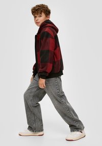 Red and black plaid fleece hoodie with black accents, paired with loose gray jeans and white sneakers with red details.
