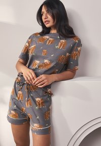 Gråt pyjamasæt med korte ærmer, der har brune ko-illustrationer med grønne detaljer; inkluderer elastik i taljen og snøre.