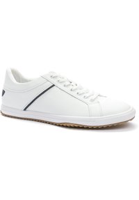 Zapatilla blanca con un upper texturizado, acentos de cuero liso y una franja azul oscura. Presenta una suela de goma con un dibujo para mayor agarre.