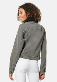 Graue Denimjacke mit einem strukturierten schwarzen Kragen, konturierten Schultern und einer taillierten Passform. Verfügt über hintere Taschen und Knopfakzente.