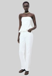 White peplum top with a fitted bodice and ruffled hem, paired with white straight-leg trousers, worn with flat sandals.