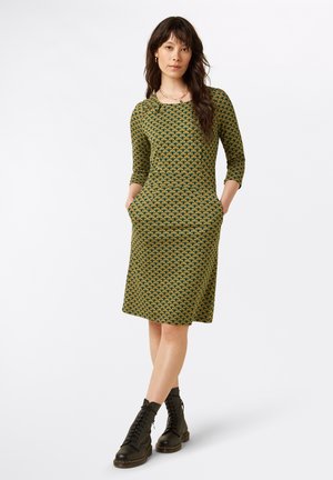 Groen patroonjurk met driekwart mouwen, ronde halslijn, zakken en een knie-lange snit; gecombineerd met zwarte enkellaarsjes.