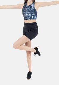 Czarne spodenki sportowe i niebieski crop top z wzorem, z bezrękawnikowym krojem, w połączeniu z czarnymi sneakersami i białymi podeszwami.