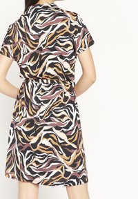 Šaty s krátkým rukávem vyrobené z lehkého materiálu a s vlnitým vzorem v černé, bílé, oranžové a hnědé barvě, se zúženým pasem a bočními kapsami.