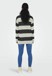 Zwart en grijs gestreepte trui, losse pasvorm, lange mouwen, geribbelde manchetten en zoom, gecombineerd met blauwe jeans en beige sneakers.