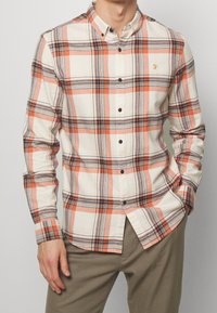 Geruite overhemd in crème, oranje en blauwe tinten; met knoopsluiting en kraag; heeft donkere knopen en een klein geborduurd logo.