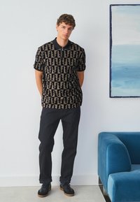 Cămașă polo cu mâneci scurte, având un model geometric în culori închise, asortată cu pantaloni negri și adidași negri. Textură netedă și detaliu cu fermoar.