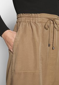 Beige midja med elastisk linning kjol med dragsko, som har två sidfickor och en mjuk, slät tygtextur.