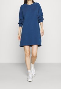 Blaues Sweatshirtkleid mit Rundhalsausschnitt und Raglanärmeln, aus weichem Stoff gefertigt. Abgerundet mit einem gestickten Logo auf der Brust.