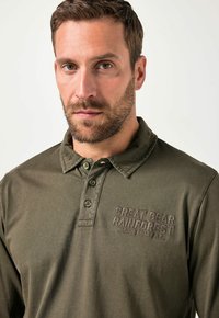 Olivgrünes Langarm-Polohemd mit Kragen, zwei Knöpfen und "GREAT BEAR RAINFOREST PACIFIC COAST B.C." in dunklem Faden gestickt.